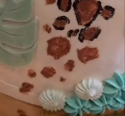 Tuvplānā tortes apakšdaļa: žirafes plankumi, zaļa lapa un krēma rozetes